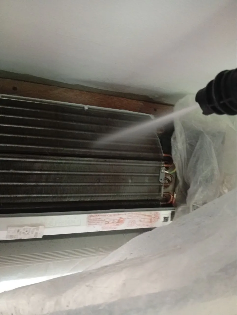 Technician pressure-washing an AC evaporator coil in Bali